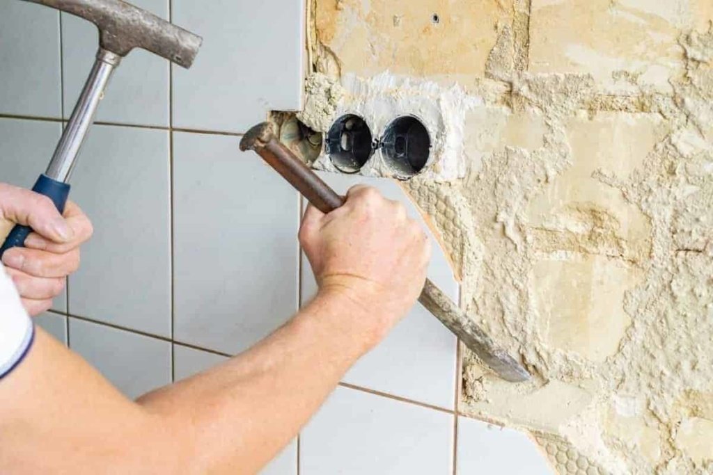 man removes wall tiles with hammer and chisel