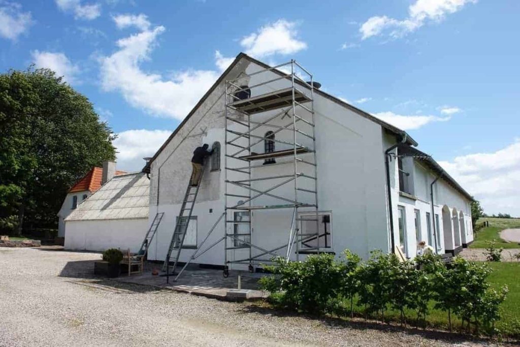 man painting house exterior with white paint