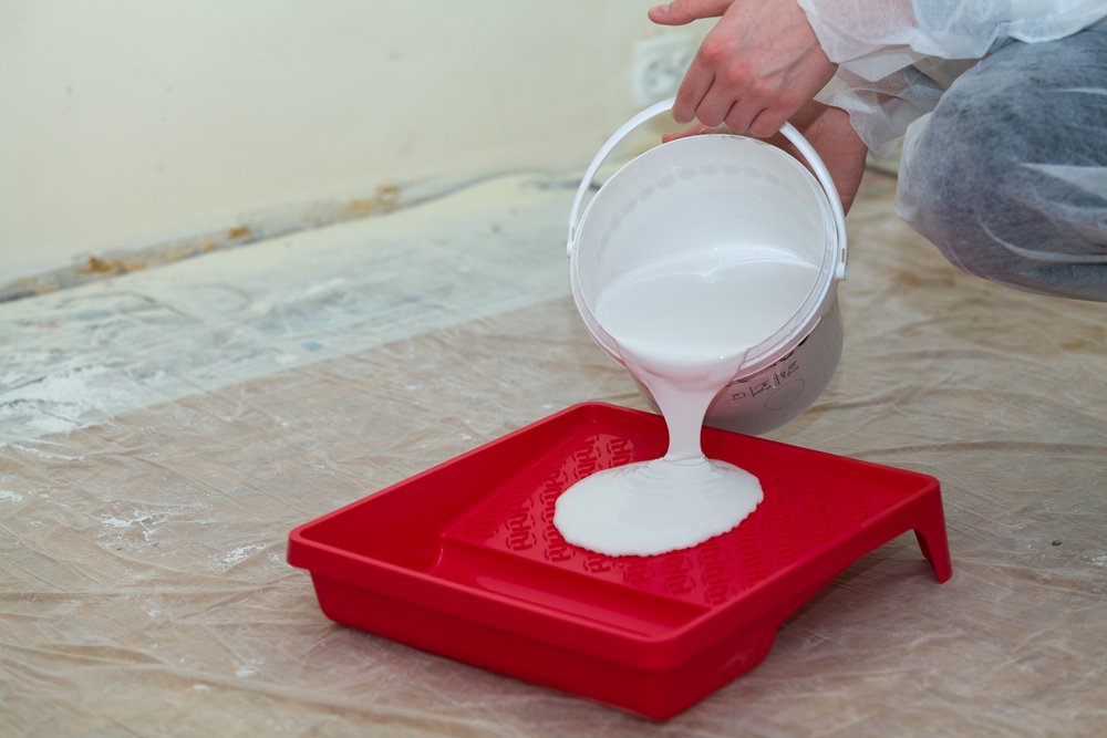 man pouring white paint onto red paint tray