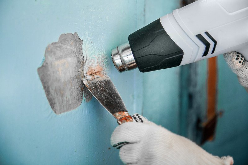 pair of hands removing old paint from concrete using heat gun and scraper