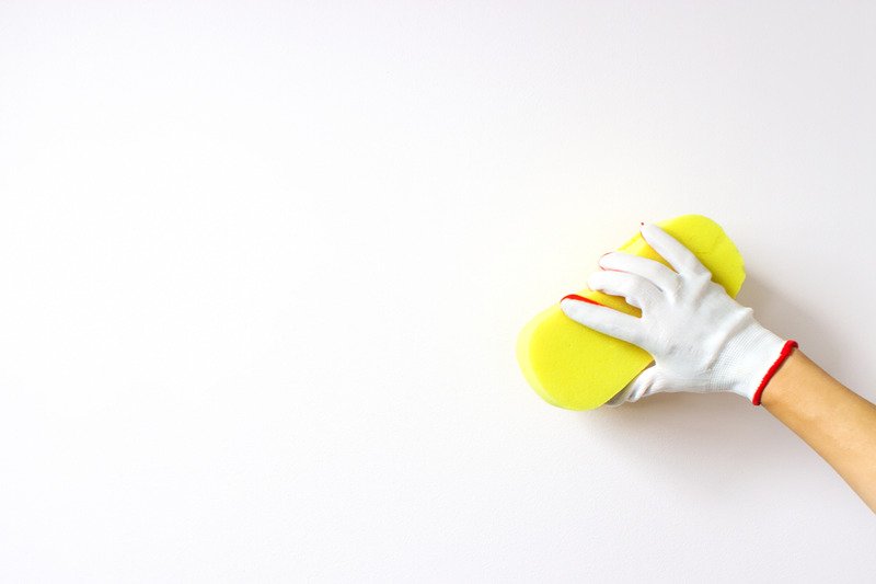 hand holds yellow sponge washing a white wall