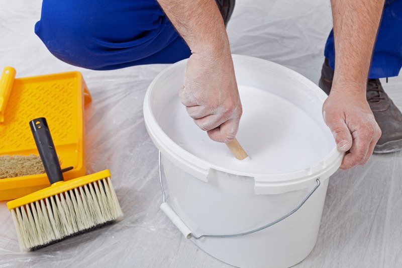 man stirring white paint in a bucket