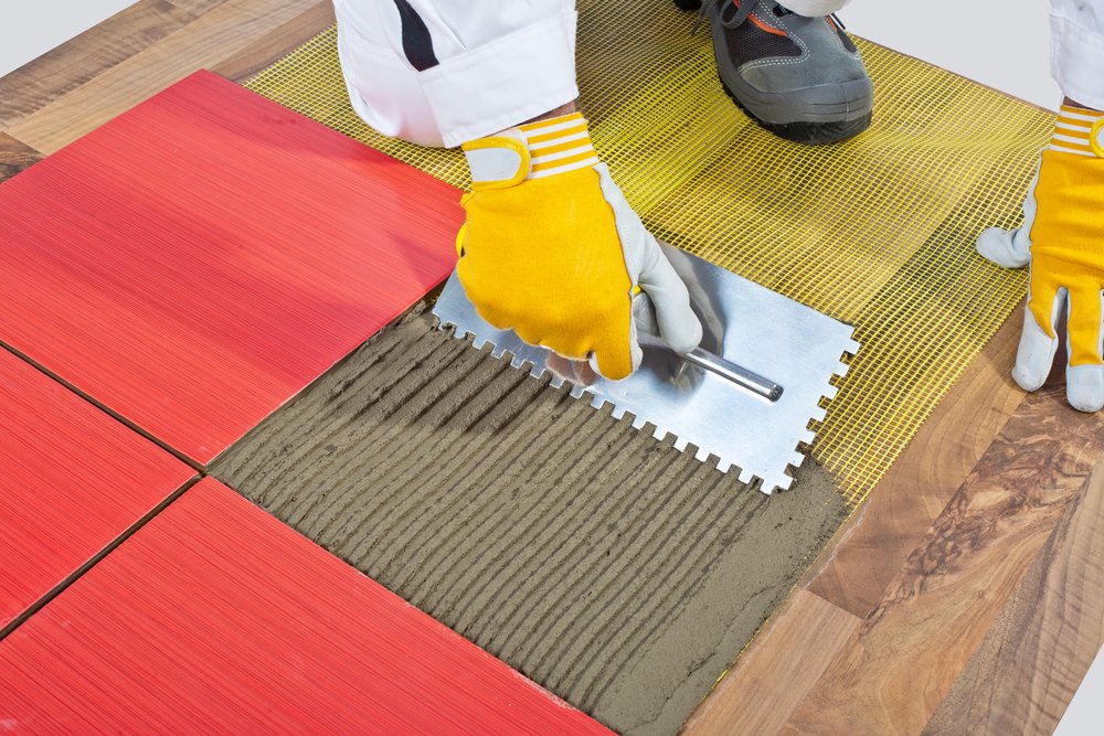 worker applying tile adhesive using tile trowel