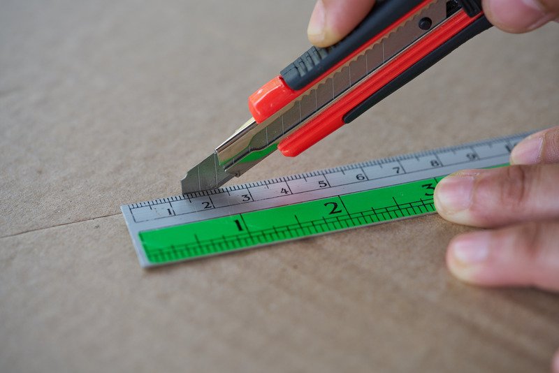 worker cutting laminate sheet using cutter guided by ruler