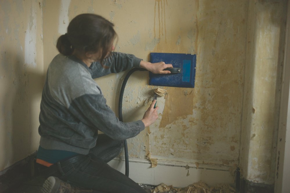 woman removing wallpaper with a steamer