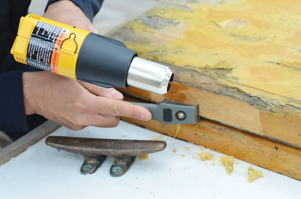 man using heat gun and scraper to remove varnish