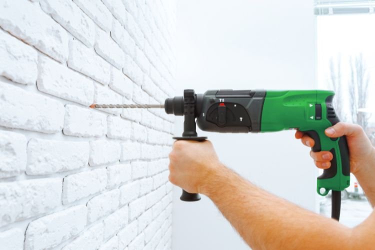 hammer drill pointed at a white brick wall