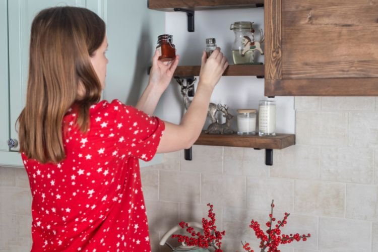 woman in a red shirt putting condiments on a kitchen shelf
