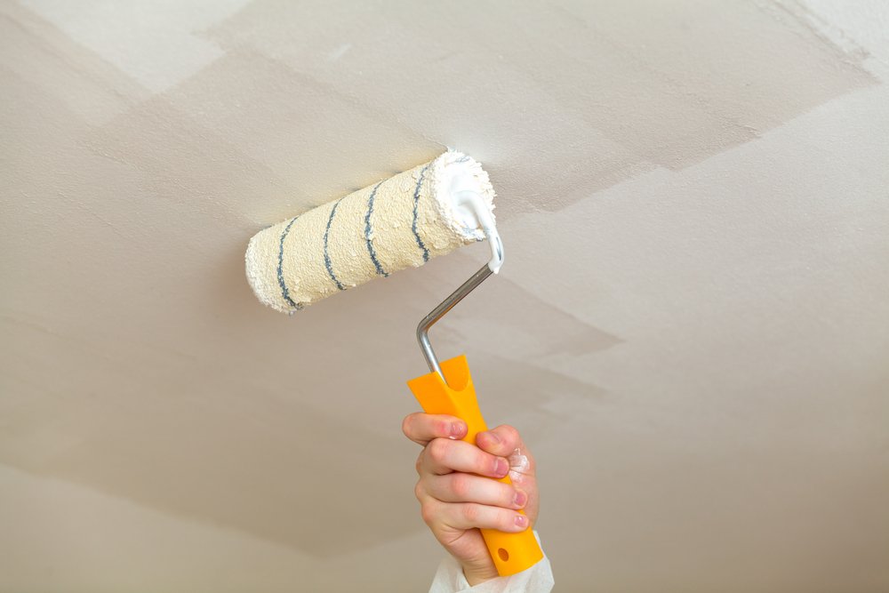 decorator painting ceiling with white paint using a roller