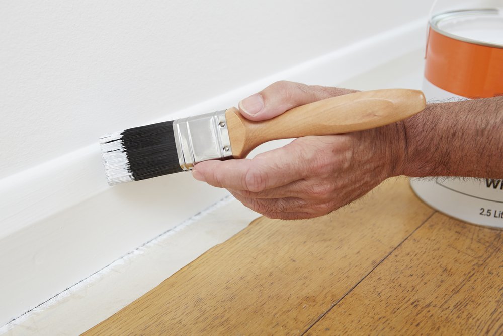 man painting skirting board with white paint