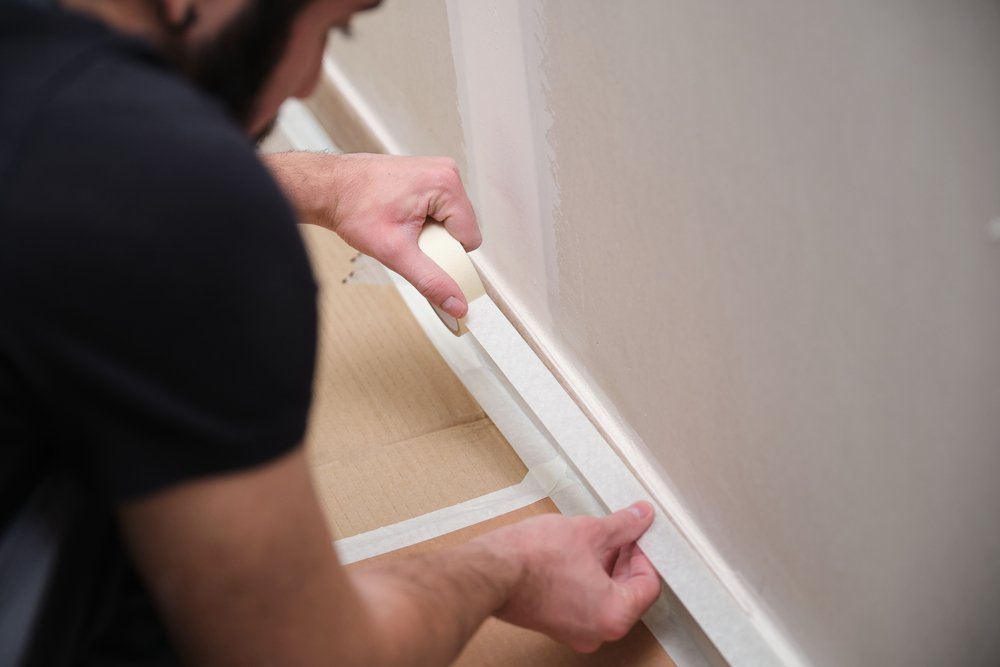 man using masking tape to cover skirting board