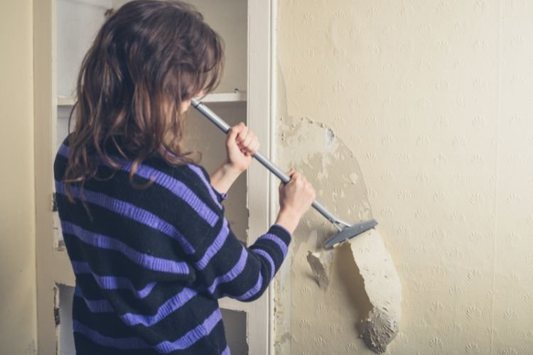 woman removing wallpaper using scraper