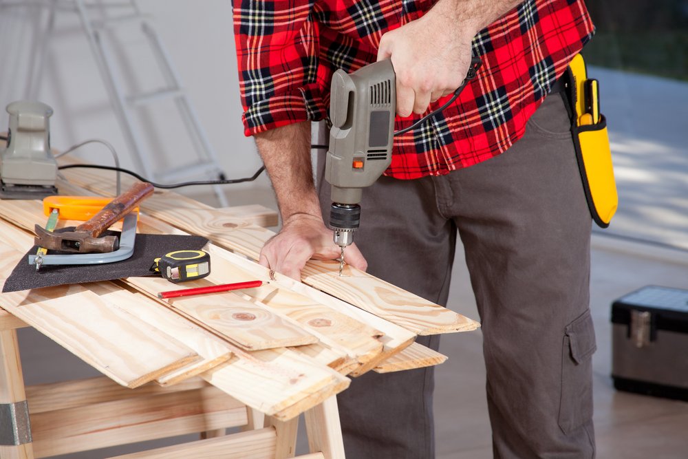 carpenter using an electric hand drill on a plank