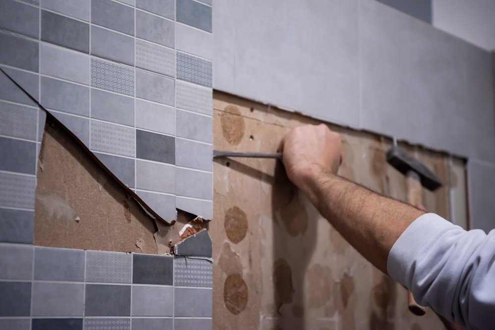 tiler removing old wall tiles in bathroom using chisel and hammer