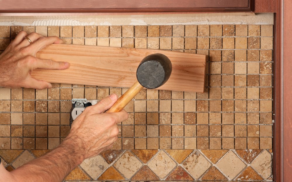 tiler flattening freshly tiled wall using rubber mallet and block of wood