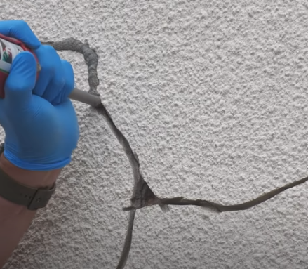 painter applying filler on cracked wall