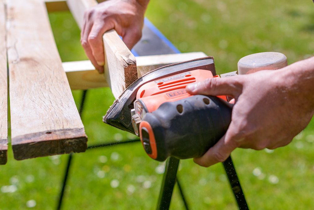 carpenter sanding wooden planks outdoors
