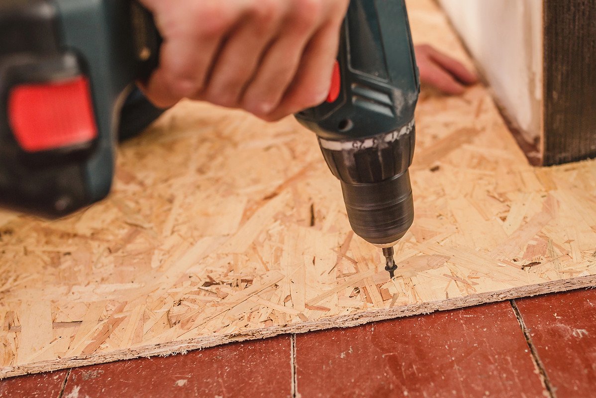 man levelling a floor using hand drill and plywood